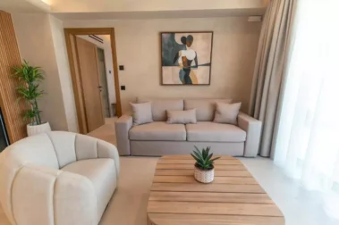 Φωτεινό σαλόνι με γκρι καναπέ, πολυθρόνα και ξύλινο τραπεζάκι, με μεγάλα παράθυρα και έργο μοντέρνας τέχνης στον τοίχο.