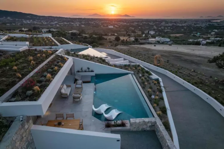 Πανοραμική άποψη βίλας με ιδιωτική πισίνα, εξωτερικό lounge και τραπέζι φαγητού, με φόντο το ηλιοβασίλεμα στο Αιγαίο.