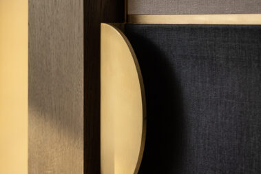 Ξύλινο γραφείο/πάγκος δωματίου ξενοδοχείου με μικρό μεταλλικό φωτιστικό, πρίζες στον τοίχο και λευκή καρέκλα στο πλάι