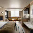 Ευρύ πλάνο σουίτας: κρεβάτι στο προσκήνιο, καθιστικό με κίτρινο καναπέ στο βάθος, ξύλινα έπιπλα και έργο τέχνης στον τοίχο.